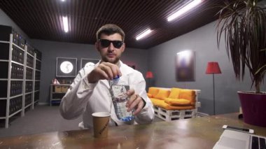 Beyaz laboratuvar önlüğü giyen sevimli adam plastik şişeden kağıt bardağa su döker