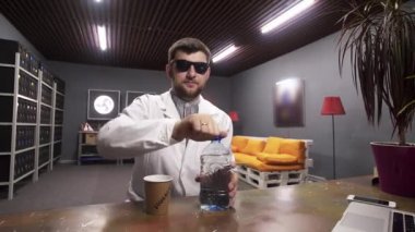 Beyaz laboratuvar önlüğü giyen sakallı erkek plastik şişeden kağıt bardağa su döküyor