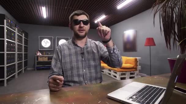 Joven con gafas de sol habla en la cámara y muestra signos con los dedos — Vídeo de stock