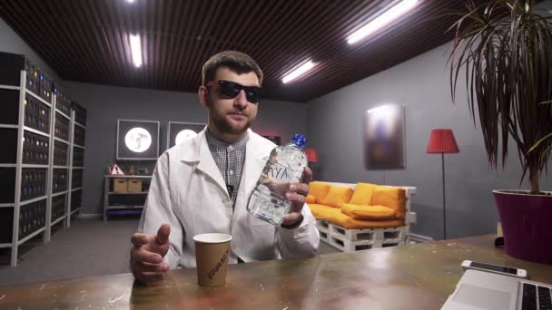 Ragazzo carismatico in camice bianco versa acqua dalla bottiglia di plastica nel bicchiere di carta — Video Stock