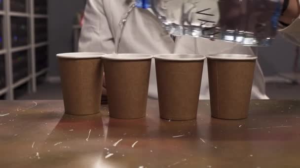 白いラボコートの男の手は、4つの紙コップにペットボトルから水を注ぎます — ストック動画