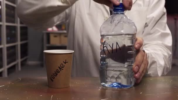 Hombre con bata de laboratorio blanca vierte agua de la botella de plástico a la taza de papel marrón — Vídeos de Stock