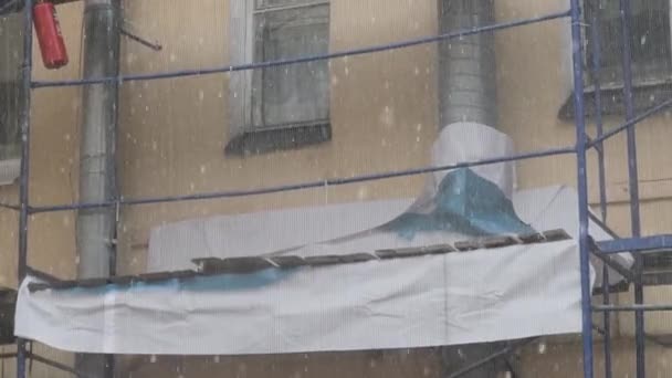 Kış kar yağışı gününde beyaz inşaat ağı ile kaplı metalik iskele — Stok video