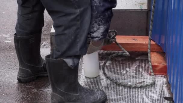 Männlicher Arbeiter in schwarzen Gummistiefeln bindet weiße Flasche mit dickem Seil zusammen — Stockvideo