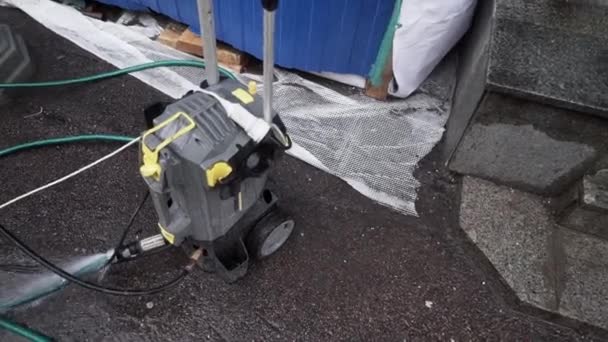 Малый механический насос с подключенными шлангами размещается на асфальтовом грунте — стоковое видео