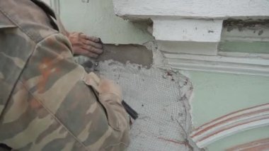 Workers hands fasten metallic wire net on green wall by nailing it with hammer