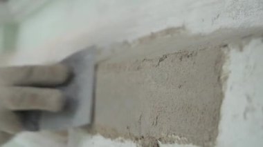 Workers hands wearing gloves accurately plaster grey wall with spackle knife