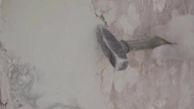 Worker hand in white gloves uses small hammer for hitting piece of facade wall