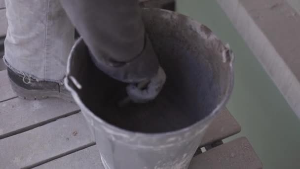 Construction worker takes out wet concrete mass with paint brush from bucket — Stock Video