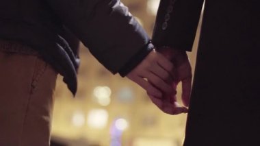 İki erkek dışarıda durup soğuk kış akşamı sokağında el ele tutuşuyorlar.