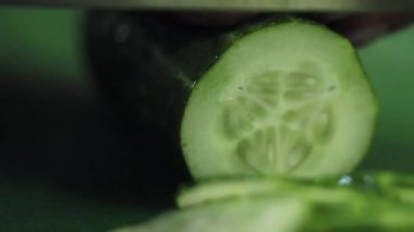 Yeşil mutfak masasında büyük keskin bıçakla dilimlenmiş salatalık closeup.