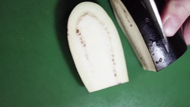Closeup de berinjela sendo fatiada com grande faca afiada na mesa de cozinha verde . — Vídeo de Stock