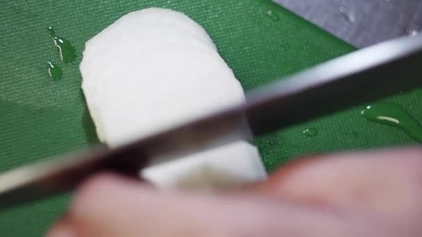 Légume blanc est coupé en anneaux avec couteau tranchant sur la table de cuisine verte . — Video