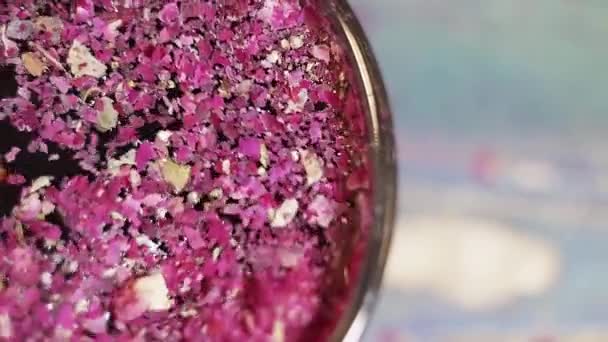Кусочки сушеных фиолетовых лепестков цветов перемешиваются ложкой в стеклянной чаше — стоковое видео