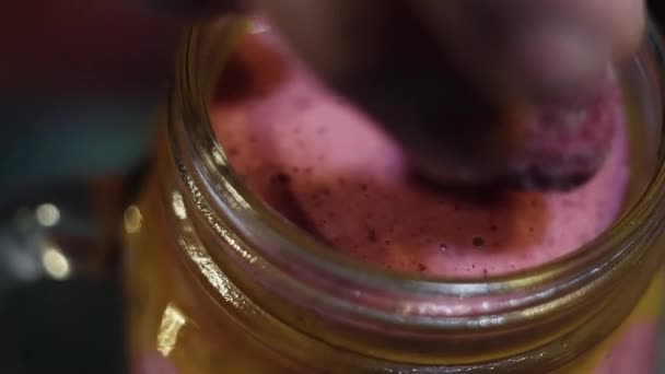 Vista macro de mão colocando única framboesa na superfície da massa rosa no frasco de vidro — Vídeo de Stock
