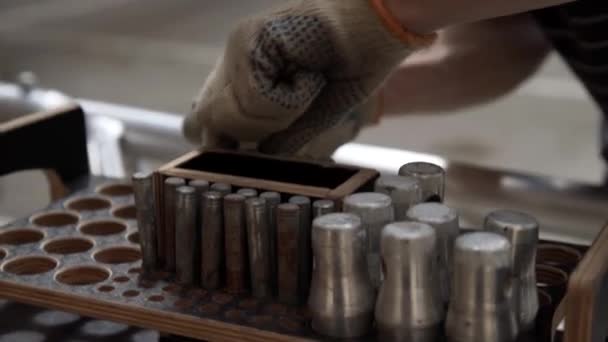 Hand in handschoenen neemt cylindrische metalen pinnen van houten kist met ronde gaten. — Stockvideo