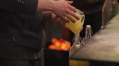 Siyah giyimli adam selofan paketinden cam şişeye portakal suyu döküyor