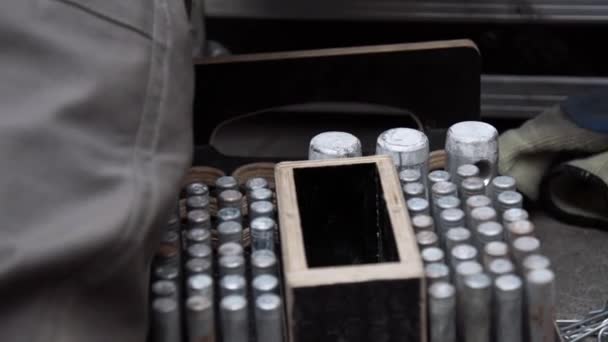 Mano de los trabajadores pone clavijas metálicas cilindro en caja de madera con agujeros redondos . — Vídeo de stock