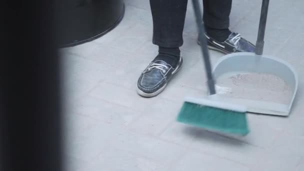 Alguien que usa zapatillas de deporte está barriendo los escombros del piso blanco en el basurero. . — Vídeo de stock