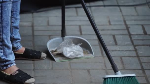 Kot giyen kadın beyaz zemindeki döküntüleri sokaktaki faraşlara süpürüyor. — Stok video