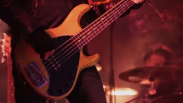 Музикант, одягнений у чорну шкіряну куртку, грає на бас-гітарі на сцені на концерті . — стокове відео