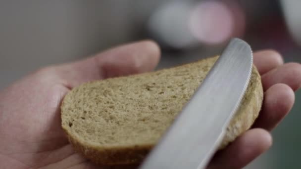Μακρο θέα των αρσενικών χεριών αργά διασκορπίσει βούτυρο σε απαγόρευση καφέ ψωμί στην κουζίνα. — Αρχείο Βίντεο