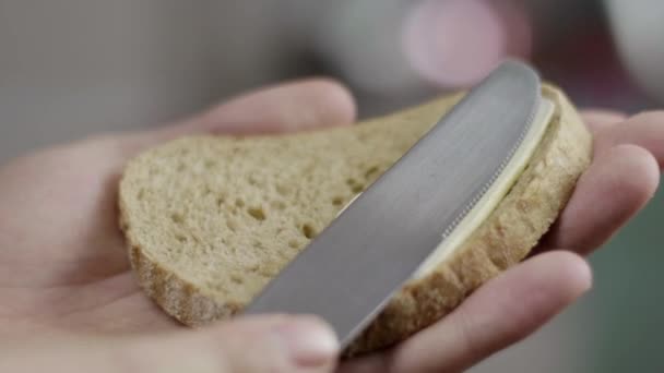 As mãos masculinas lentamente e cuidadosamente estendem a manteiga no pão marrom de proibição na cozinha . — Vídeo de Stock