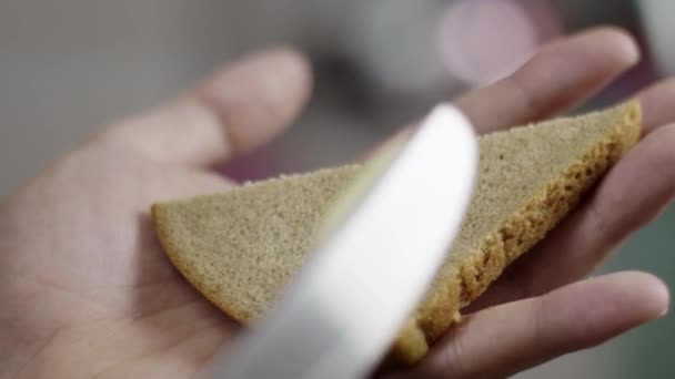 Male hands spreading butter on triangular bread slice in kitchen in slow motion. — Stock Video