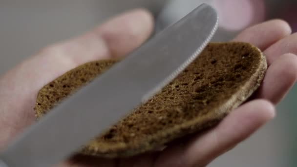 Persons hands spread butter on slice of brown bread in kitchen in slow motion. — Stock Video