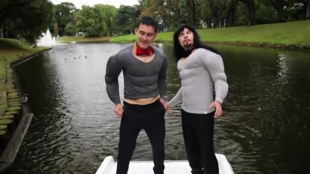 Két fiatal férfi hamis izommellkas és a fegyverek párnázott jelmezek állni a hajón — Stock videók
