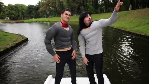 Two attractive men in fake muscle chest and arms padded costumes sing in boat — Stock Video