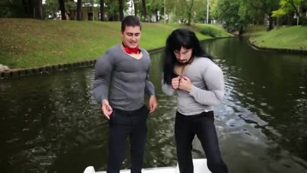Двоє привабливих хлопців, одягнених у підроблені м'язи, танцюють у рухомому човні — стокове відео