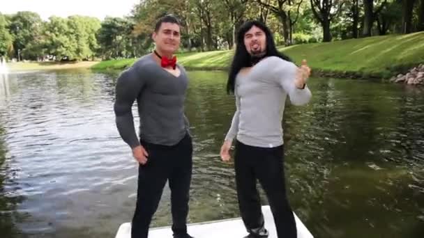 Twee grappige jongens in nep spier gewatteerde kostuums dansen en zingen in bewegende boot — Stockvideo
