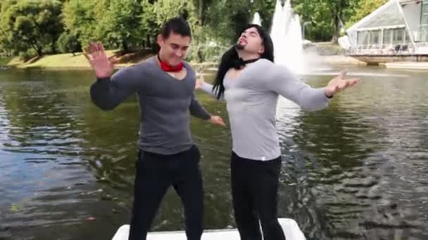 Двоє молодих смішних чоловіків у фальшивих м'язових костюмах харизматично танцюють у човні — стокове відео