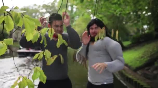 Grappige jongens in nep spier kostuums op drijvende boot hit dunne boomtakken. — Stockvideo