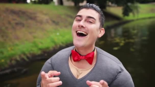Aantrekkelijke kerel met nep spier kostuum en rode vlinderdas zingt in drijvende boot — Stockvideo