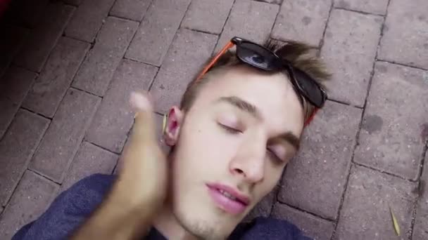 Handsome fainted guy is lying on concrete ground and being awaken with slaps — Stock Video