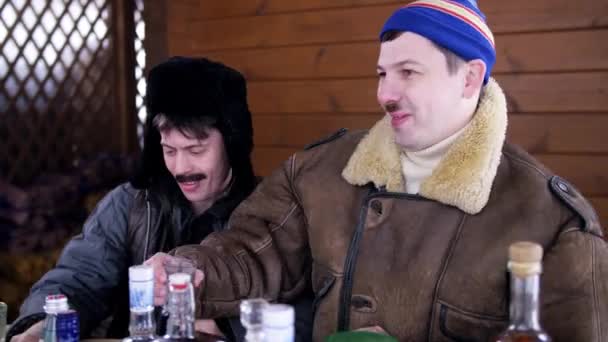 Kışlık kıyafetler ve şapkalar giyen iki adam masanın etrafında oturup yemek ve konuşma yla sohbet ediyor. — Stok video