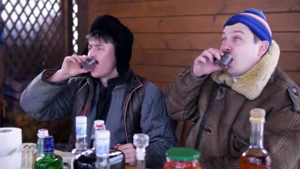 Homens amigos colocar roupas de inverno sentar em torno da mesa, rir e beber álcool . — Vídeo de Stock