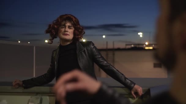 Мужчина, одетый как женщина в черную куртку и парик, поет на улице — стоковое видео