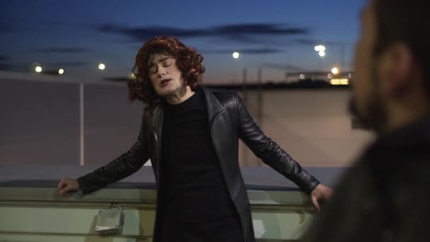 Смішний чоловік, одягнений як жінка, одягнений у чорний одяг та перуку, співає надворі — стокове відео