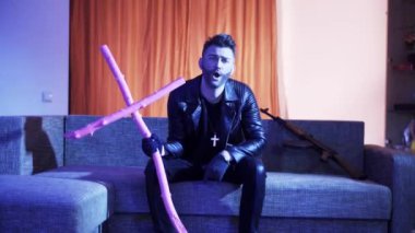 Deri ceketli şık saçları yla güzel görünümlü adam kanepeye oturur ve şarkı lar.