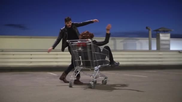 Hombre con chaqueta empuja a otro hombre vestido como mujer sentado en el carrito de la compra . — Vídeos de Stock