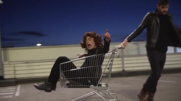 Lindo hombre juguetonamente tira del carrito de la compra con otro tipo vestido como mujer en ella — Vídeos de Stock