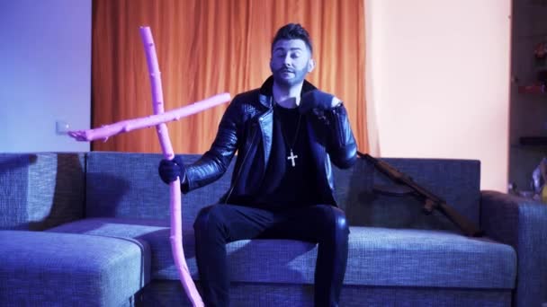 Knappe man gekleed in zwart lederen jas sitson sofa, dansen en zingt. — Stockvideo