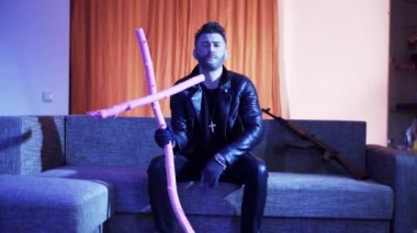 Siyah deri ceket giyen yakışıklı genç adam kanepeye oturur ve şarkı lar.