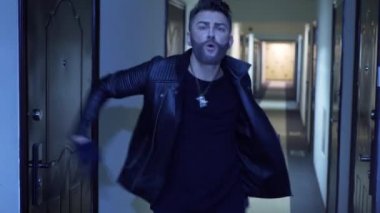 Şık saç kesimi ve jaket dansında takma sakalı olan genç adam dar koridorda dans ediyor.
