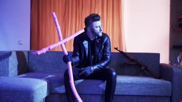 Sexy man with stylish hair cut in leather jacket sits on sofa and sings. — Stock Video