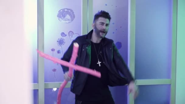 Attractive man with stylish hair cut in leather jacket dances holding pink cross — Stock Video