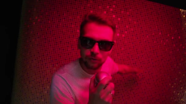 Brünetter Mann mit Sonnenbrille und weißem T-Shirt singt mit Mikrofon — Stockvideo